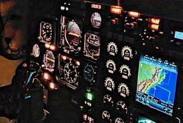 The illuminated instrument panel of an aircraft cockpit, showing various gauges and a navigation display.