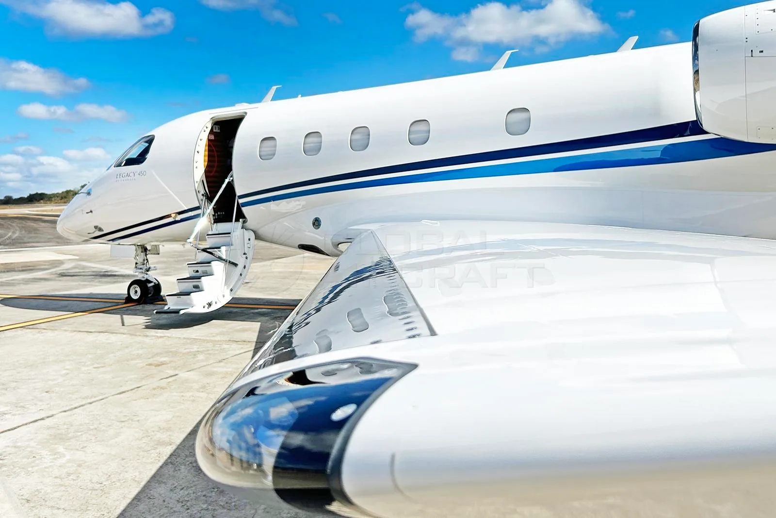 Front-side view of a white Embraer Legacy 450 business jet with its passenger door open and a reflective wing.
