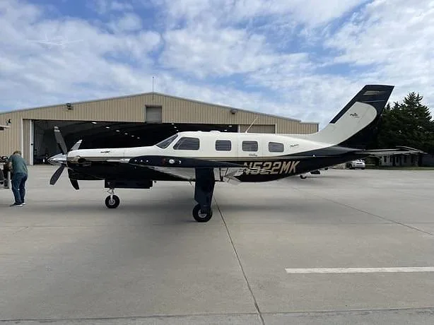 A black and white Piper M-Class aircraft, N522MK, is parked on an airfield tarmac next to a hangar.