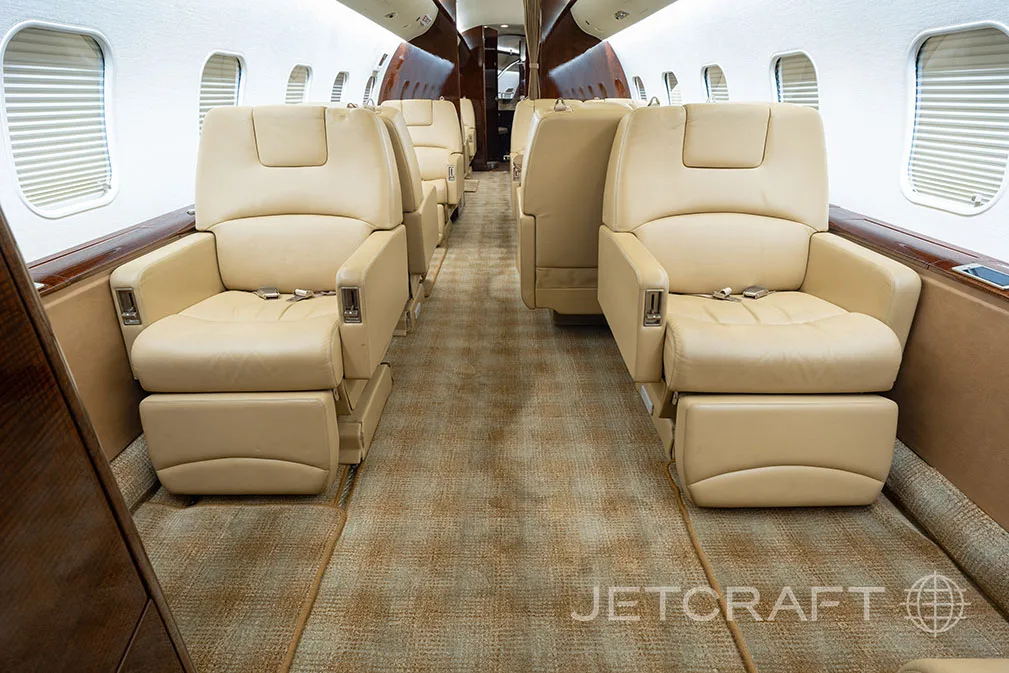 The luxurious cabin interior of a private jet with beige leather seats and a patterned carpet.