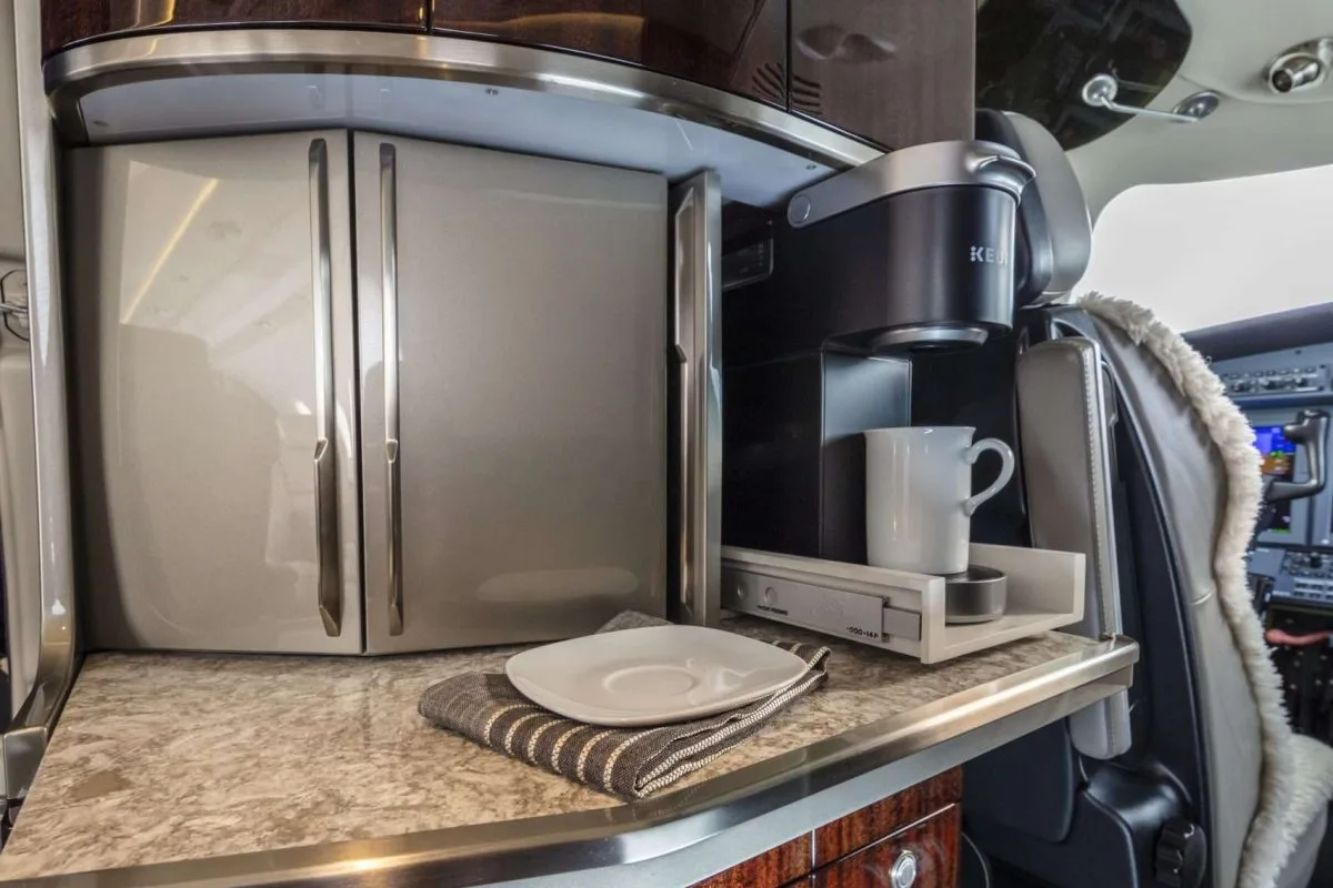 Interior view of the aircraft galley with a coffee maker and storage.
