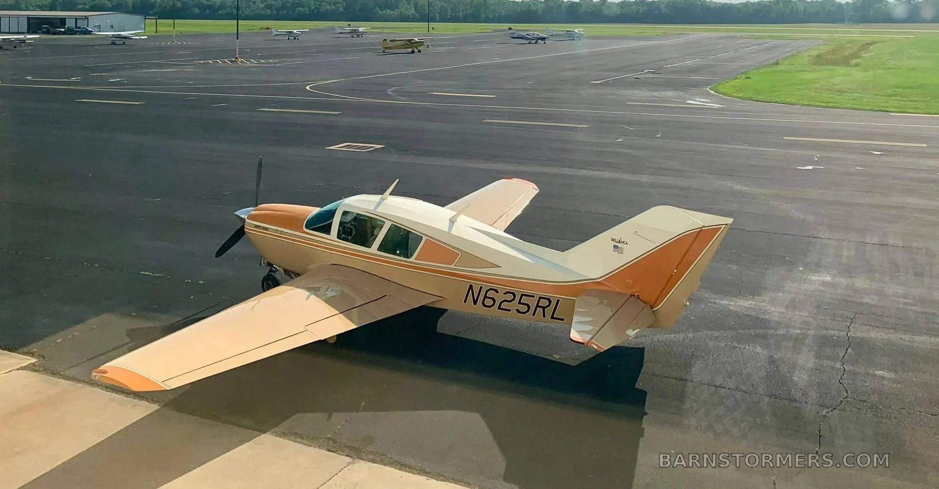 A beige and orange single-engine aircraft (N625RL) parked on an asphalt ramp at an airfield, viewed from above and behind.