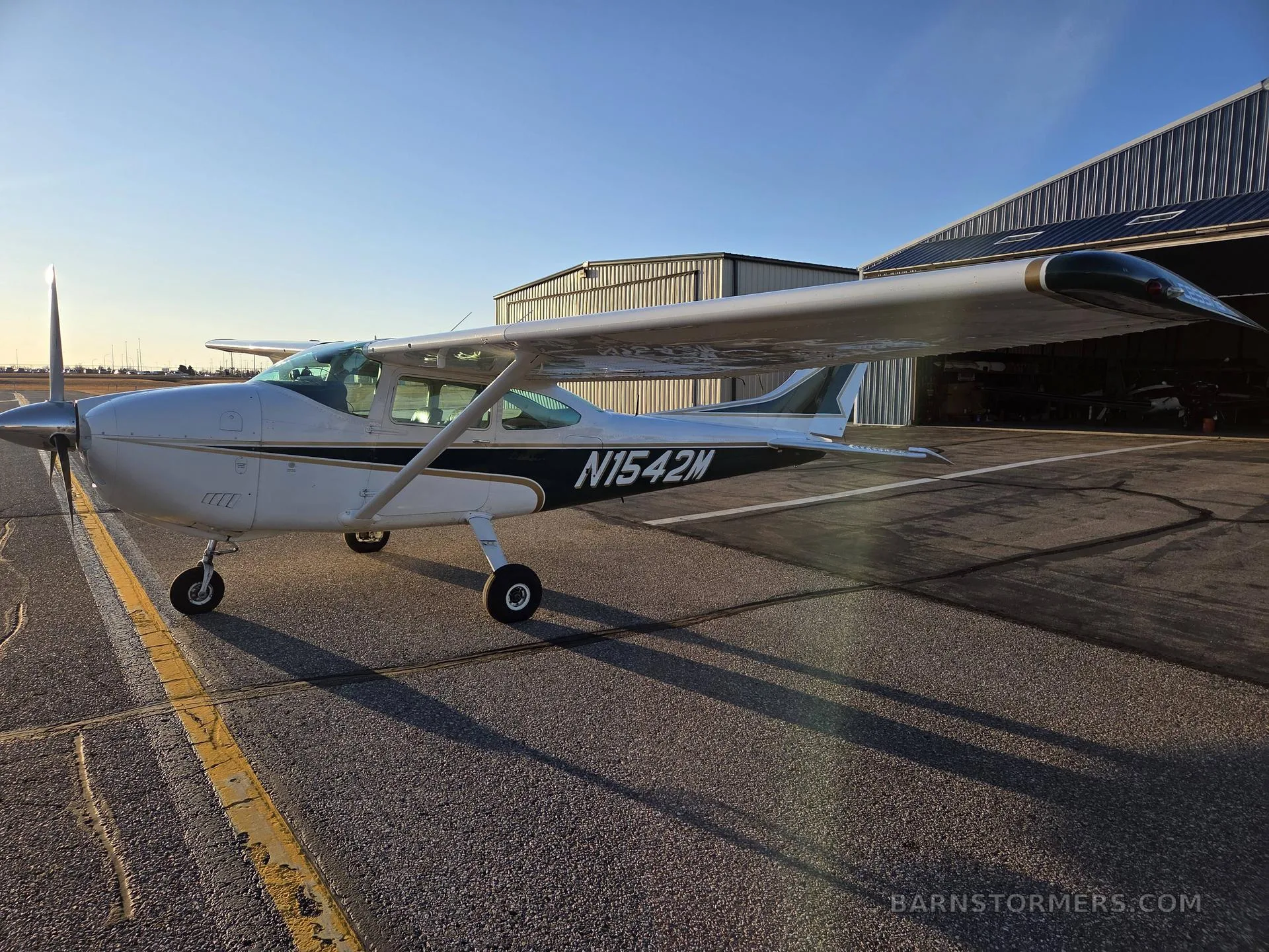 A white and green Cessna aircraft with registration N1542M parked on an airfield, viewed from the rear-left.