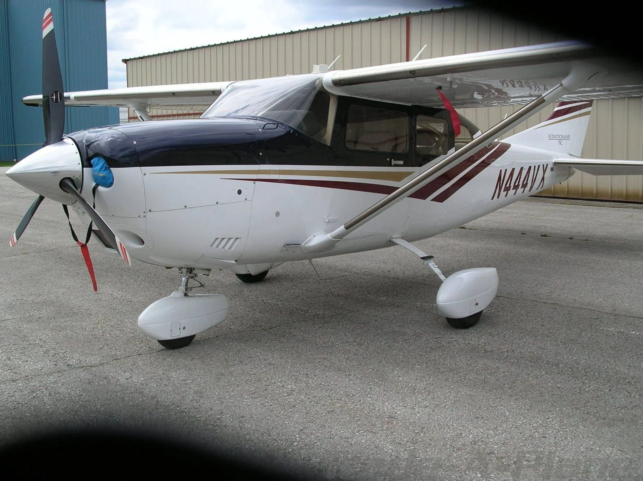 A white Cessna Stationair TC with dark blue and maroon stripes, registration N444VX, parked on an asphalt ramp.