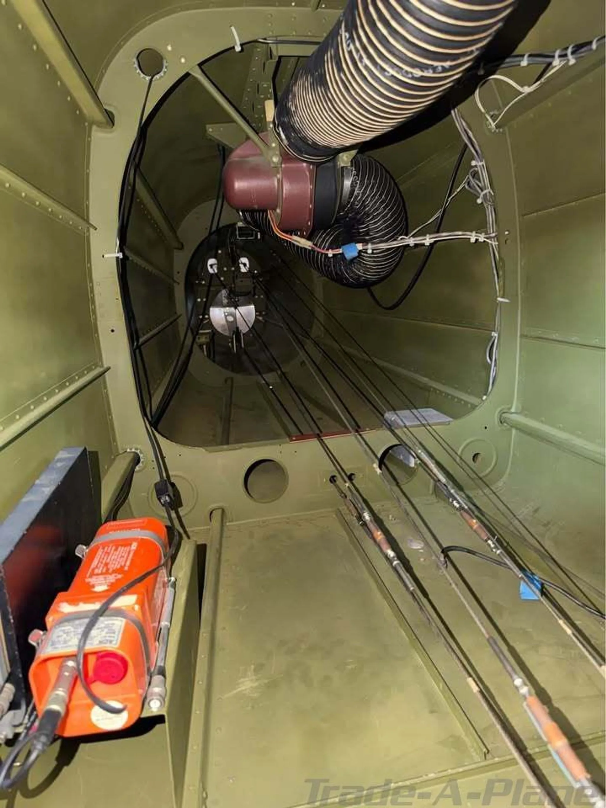 An overhead view of the aircraft's internal fuselage structure, showing wires, control cables, and an orange ELT unit.