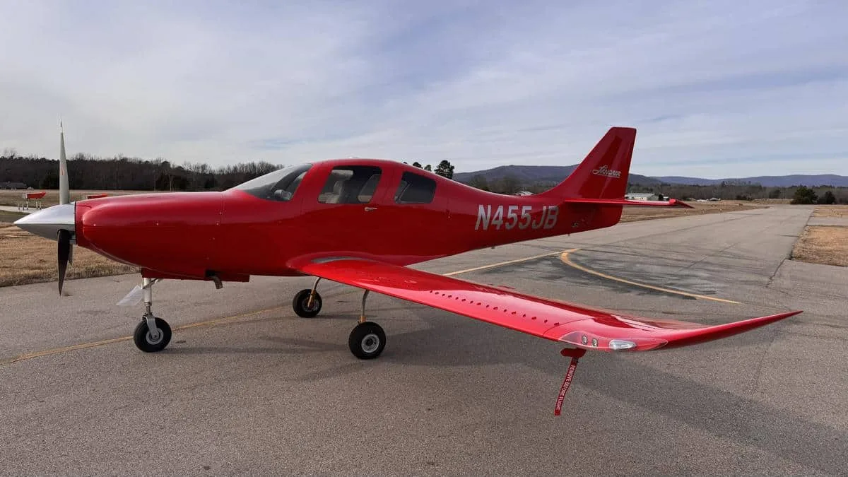 A bright red single-engine propeller aircraft, likely a Cirrus SR22, is parked on an asphalt apron with mountains in the background.