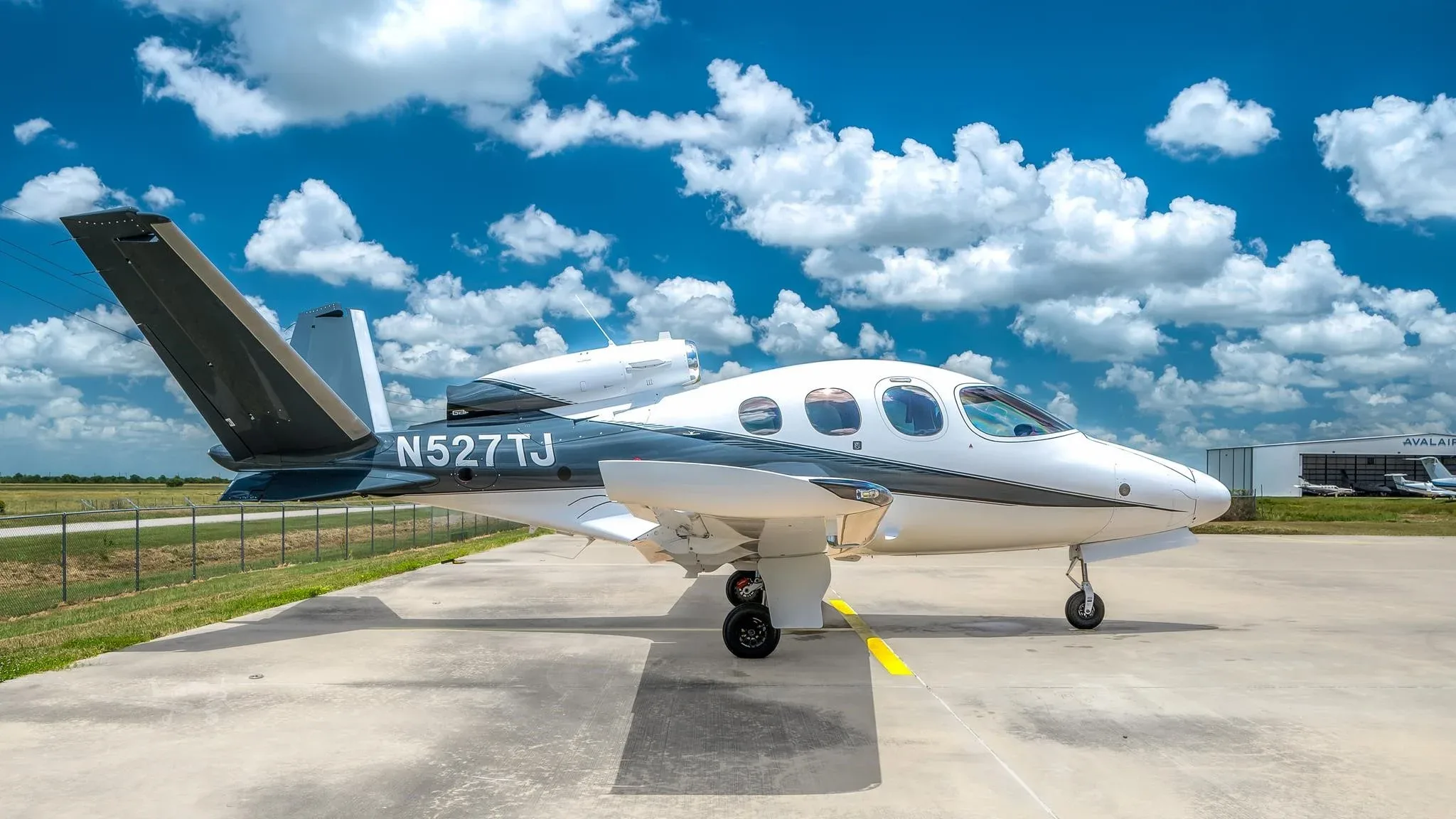 A white and dark grey Cirrus Vision Jet (SF50) with registration N527TJ parked on a tarmac under a blue sky.