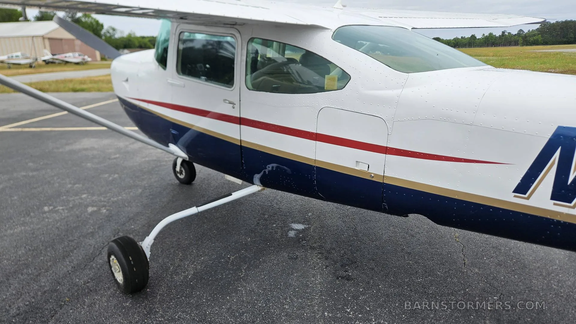 A side view of the white and blue Cessna 182 aircraft, showing the cabin windows and landing gear on the tarmac.