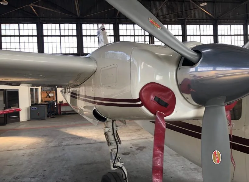 Close-up of the right engine and propeller of a white aircraft with a maroon stripe, inside a hangar.