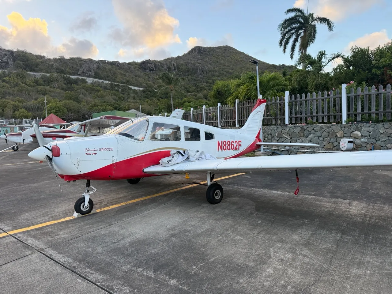 A white and red Piper Cherokee Warrior 160 HP aircraft (N8862F) parked on an airfield with mountains in the background.