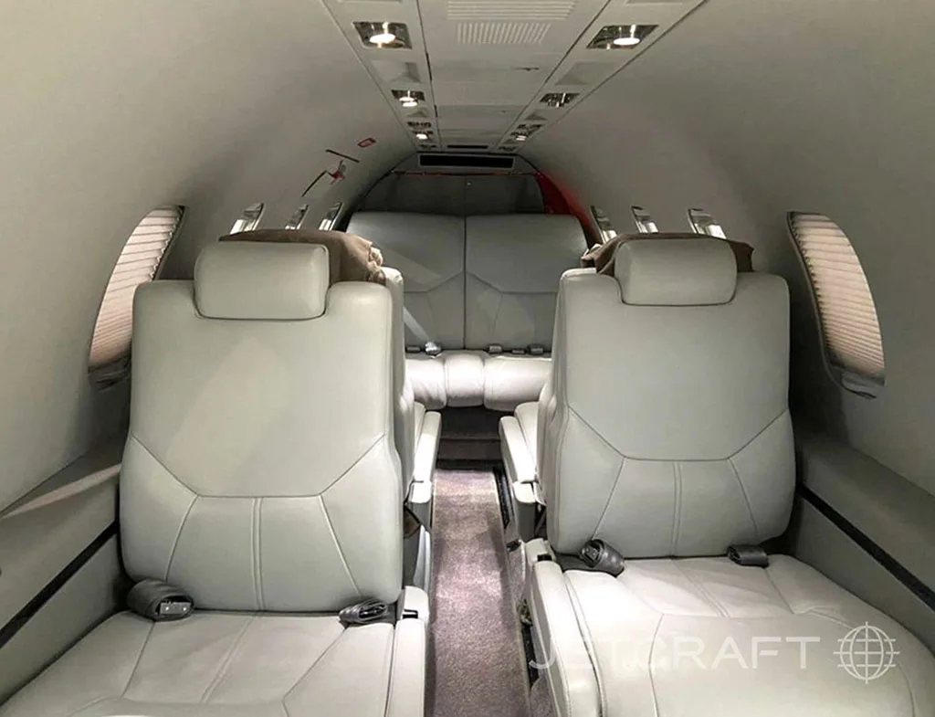 The interior cabin of a private jet featuring light grey leather seats and a two-seat bench at the rear.