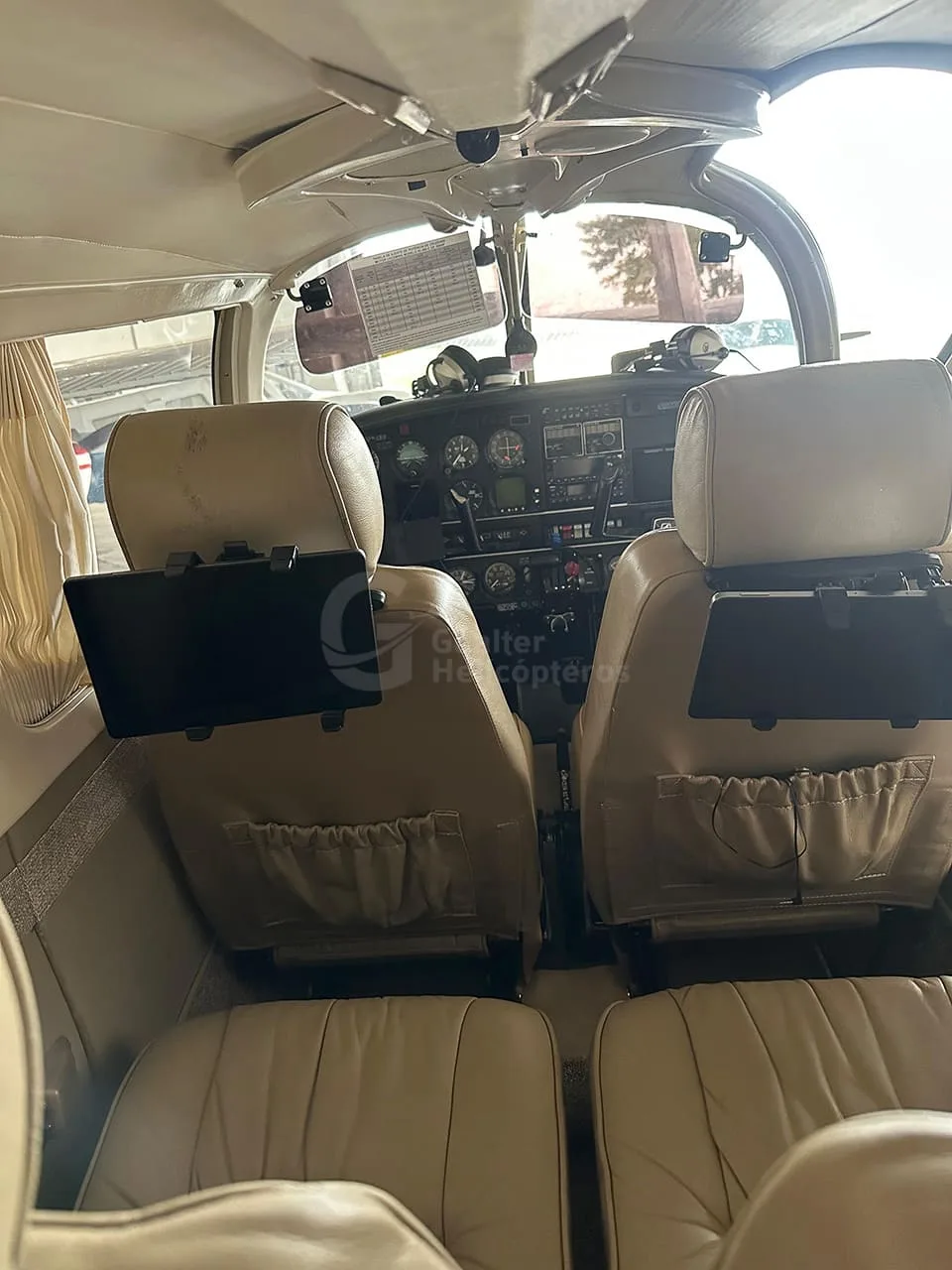 The interior cabin of a small aircraft, showing tan leather seats and the cockpit through the front seats.