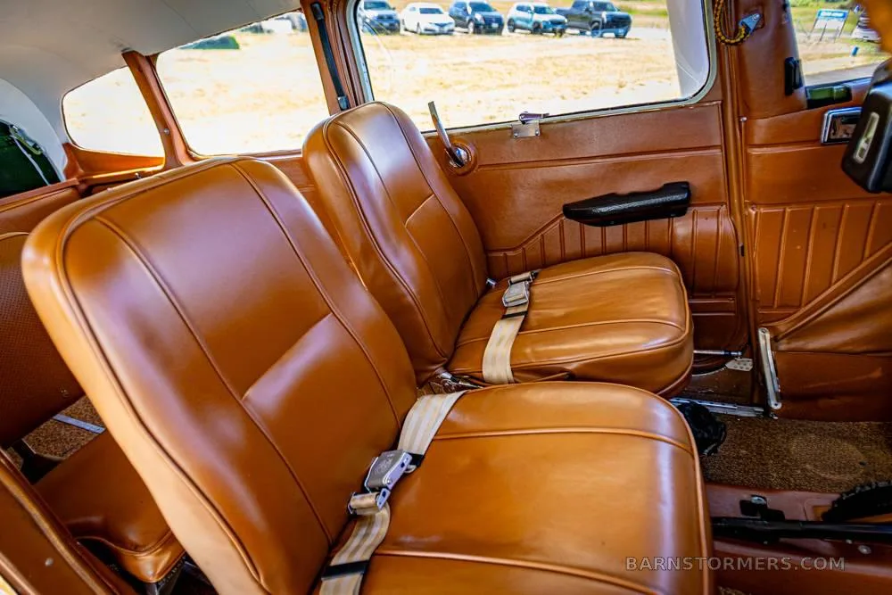 The brown leather passenger seats in the cabin of a small aircraft, with a view of cars outside the window.