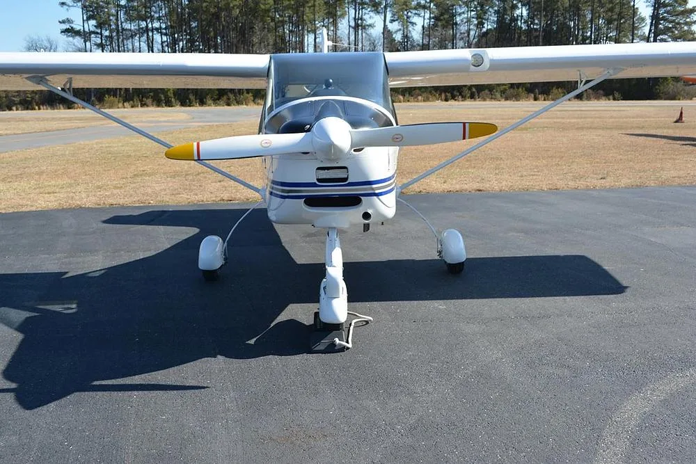A head-on view of a white Tecnam Light Sport aircraft with a propeller, parked on an asphalt ramp.