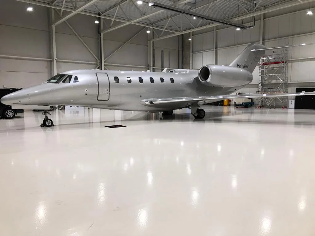 A silver private jet (PH-NNX) parked inside a brightly lit hangar.
