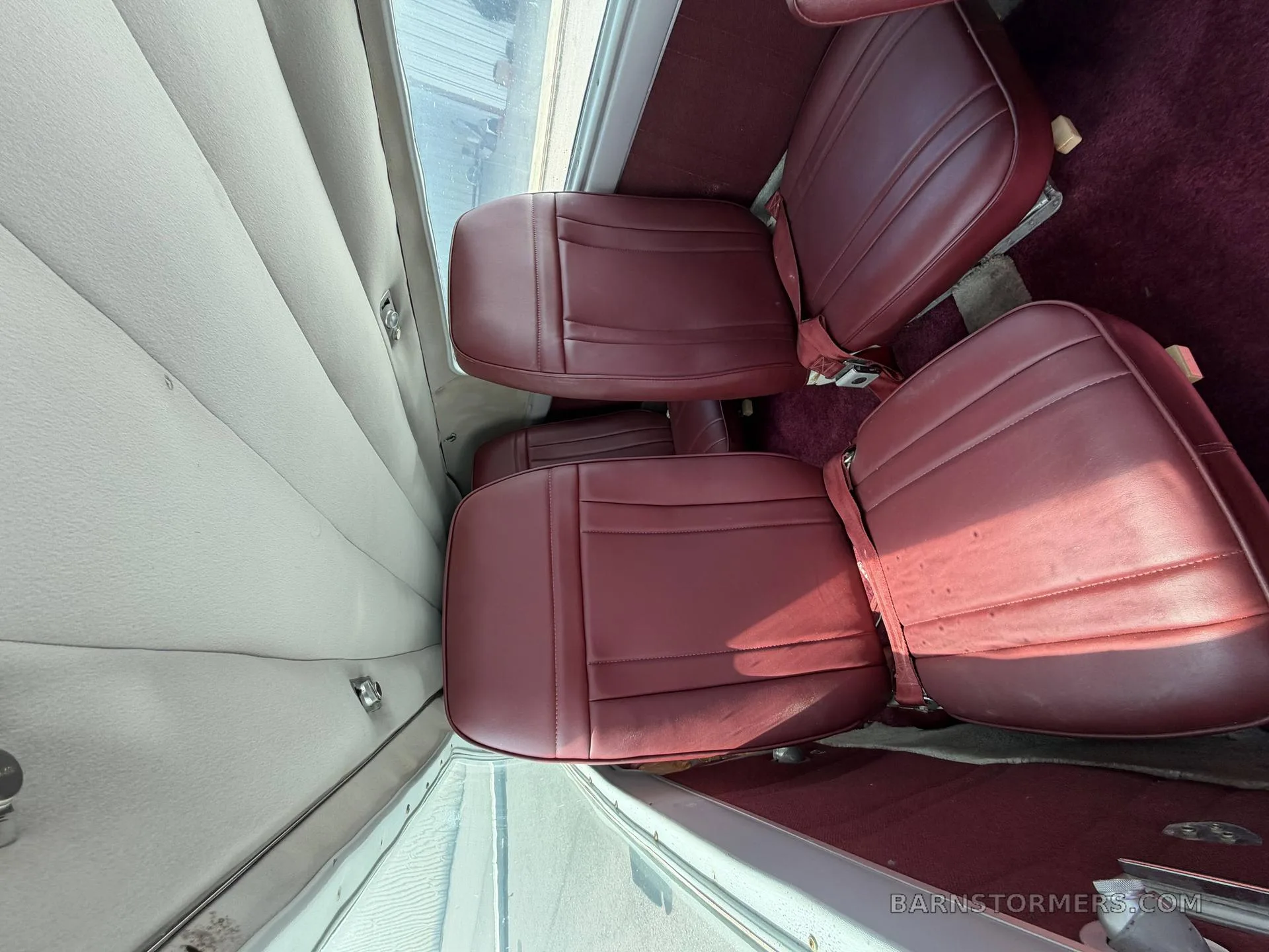 A view of the aircraft's cabin interior, showing two rows of red leather passenger seats.