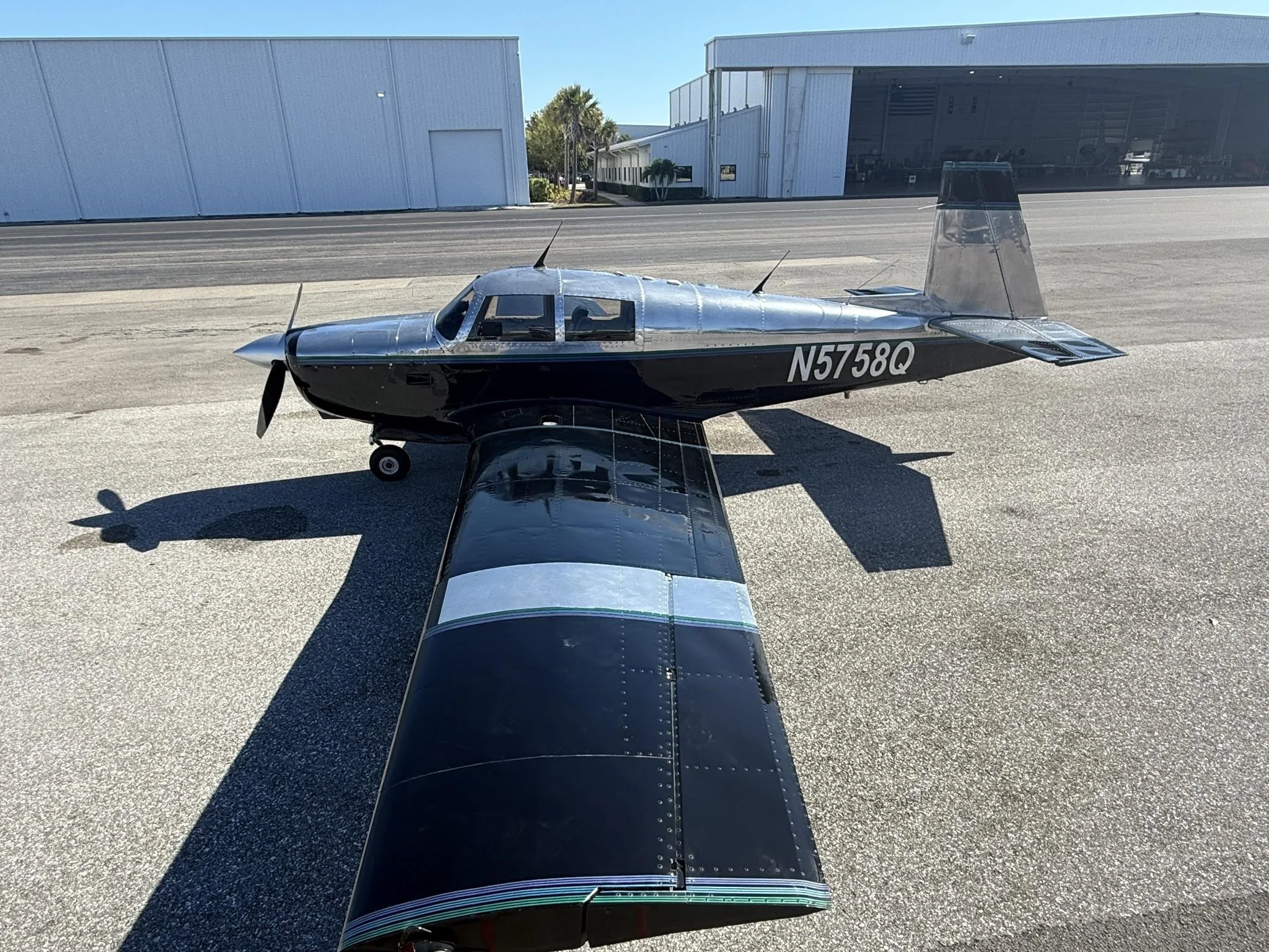A black and silver Mooney M20 aircraft, N5758Q, parked on an asphalt tarmac with hangars in the background.
