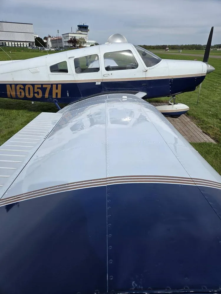 An overhead view of the wing and fuselage of the Piper PA-28 Cherokee, registration N6057H, with an air traffic control tower in the background.