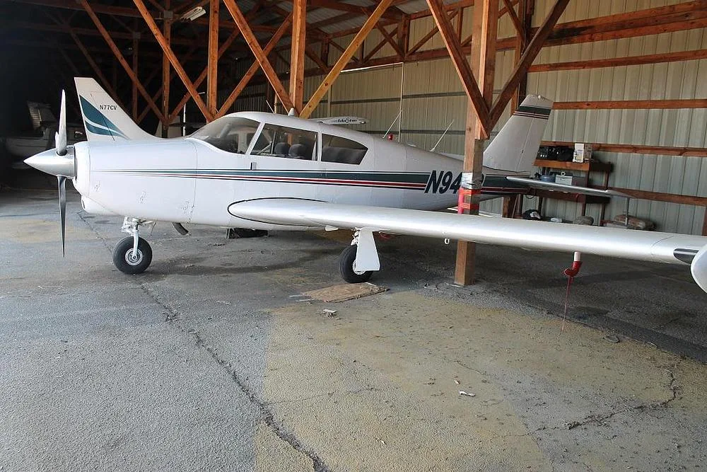 A white single-engine propeller aircraft, N949P, with green and red stripes, parked in a hangar.