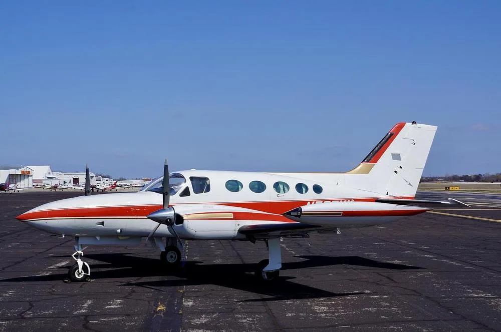 A white and red Cessna 400 series twin-engine aircraft, registration N555MY, is parked on an asphalt tarmac under a clear blue sky, viewed from the left side.