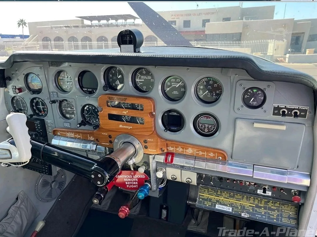 The cockpit instrument panel of a Beechcraft Bonanza, featuring analog gauges and a wooden trim panel.