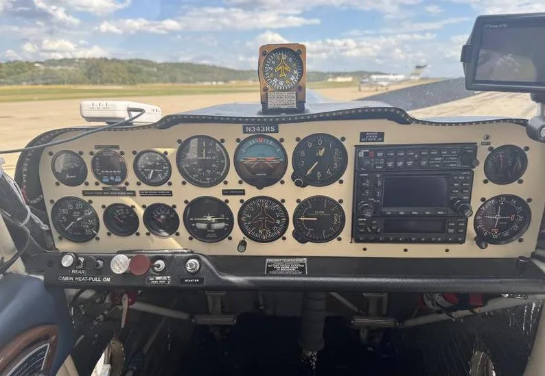 The instrument panel of a light aircraft, featuring analog gauges and a modern radio stack, with a runway visible through the windshield.