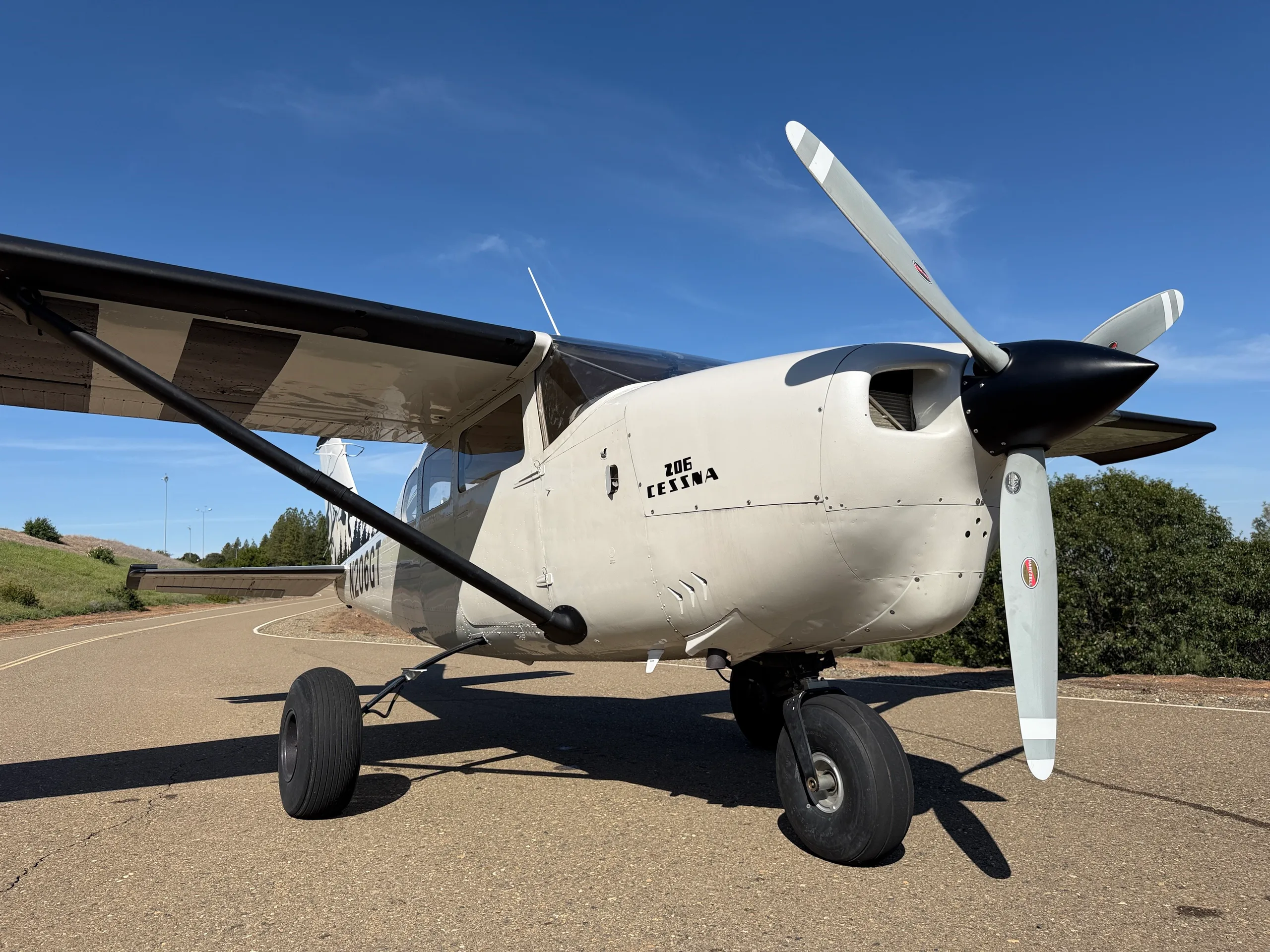 Close-up front view of a white Cessna 206 with black and white striped wings and a large propeller, parked on an asphalt strip.