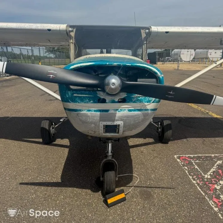 Front view of a Cessna 150 with a weathered blue and white paint scheme, parked on an asphalt ramp.