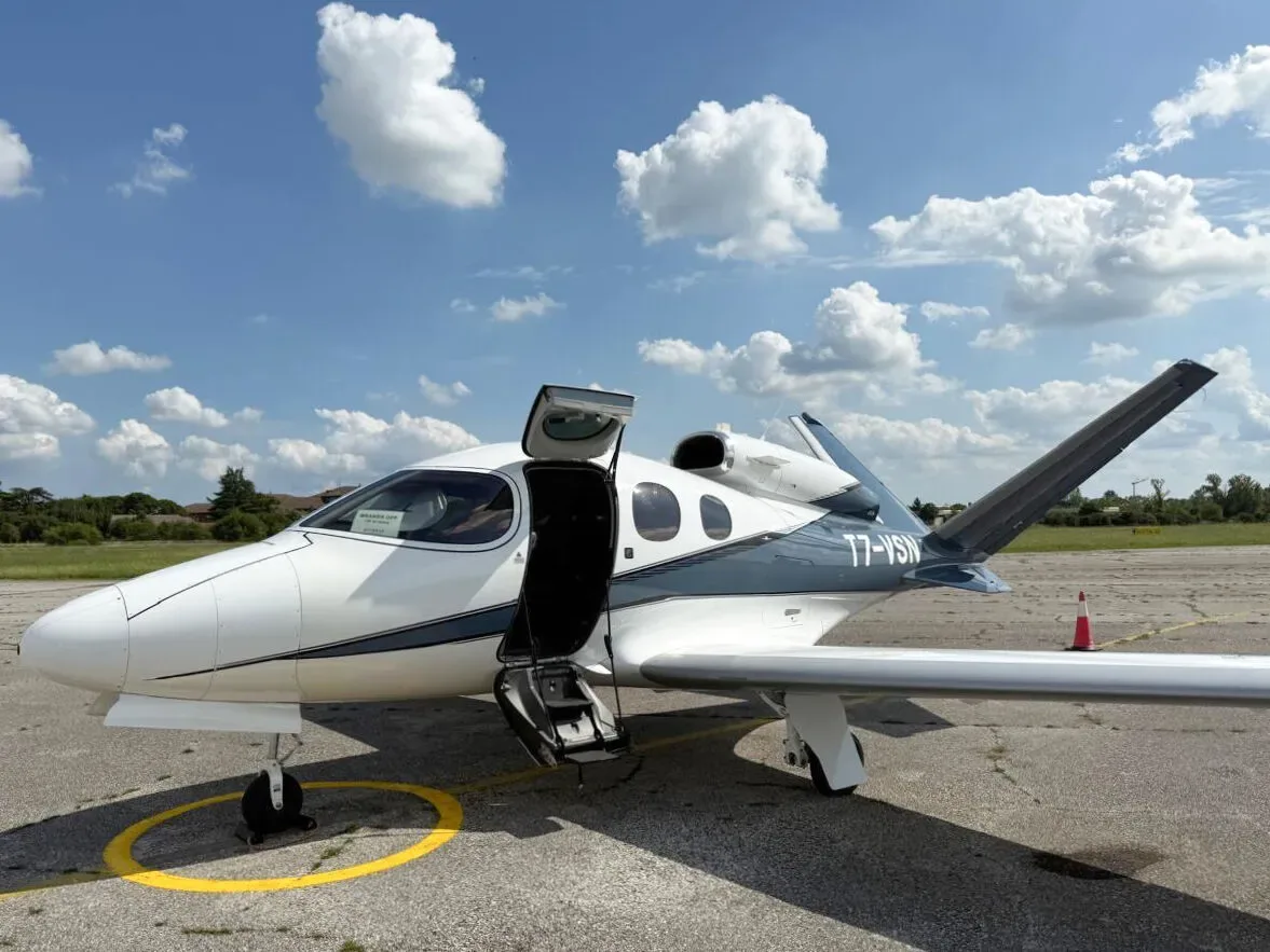 A white and dark blue Cirrus Vision Jet (T7-VSN) parked on an airfield with its main cabin door open.