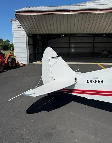 The tail section of a white aircraft with red stripes, showing the N-number N98959, parked on an asphalt tarmac.