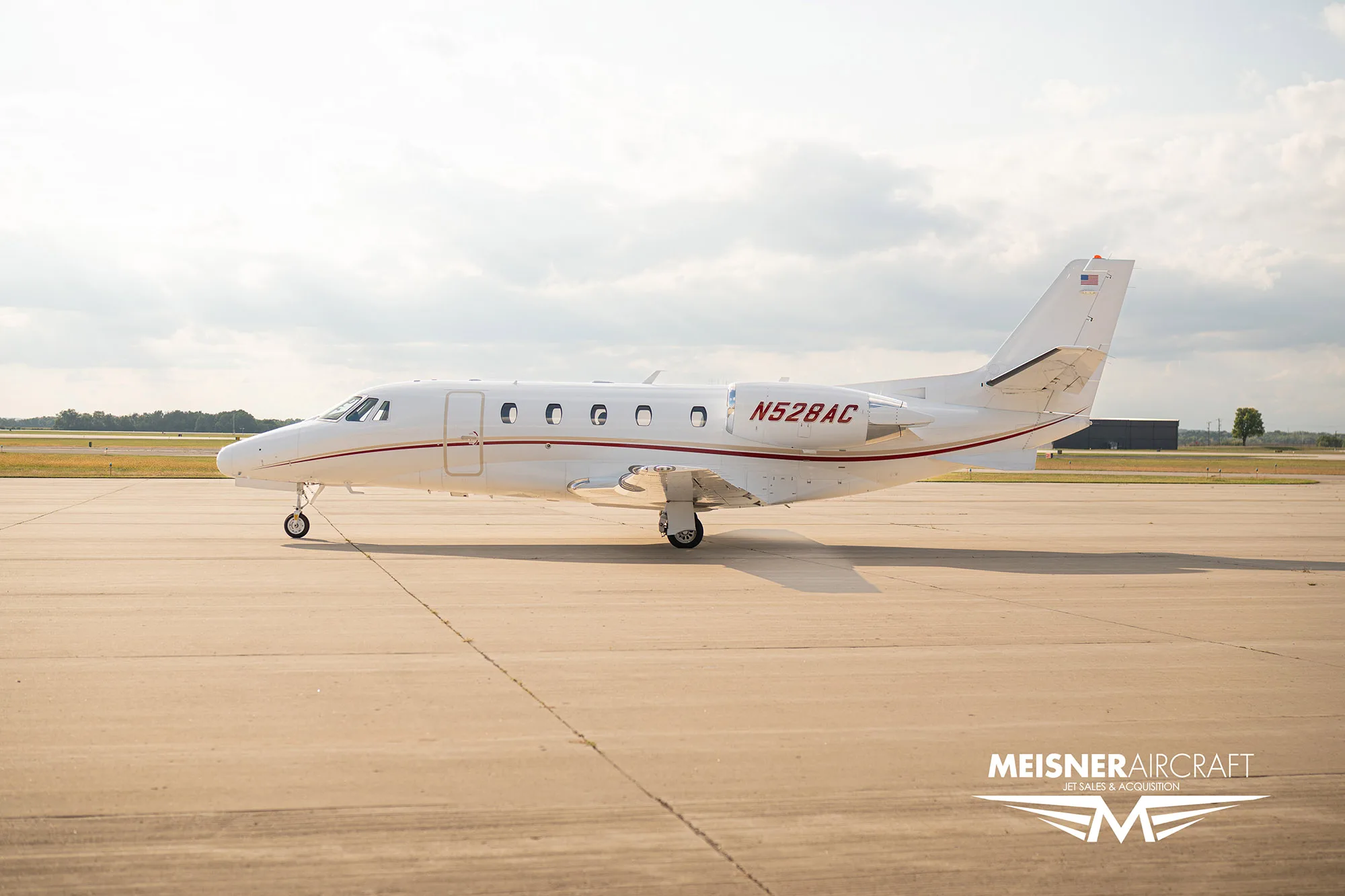 A white business jet with red stripes and registration N528AC parked on an airfield, with a 'Meisner Aircraft' logo.
