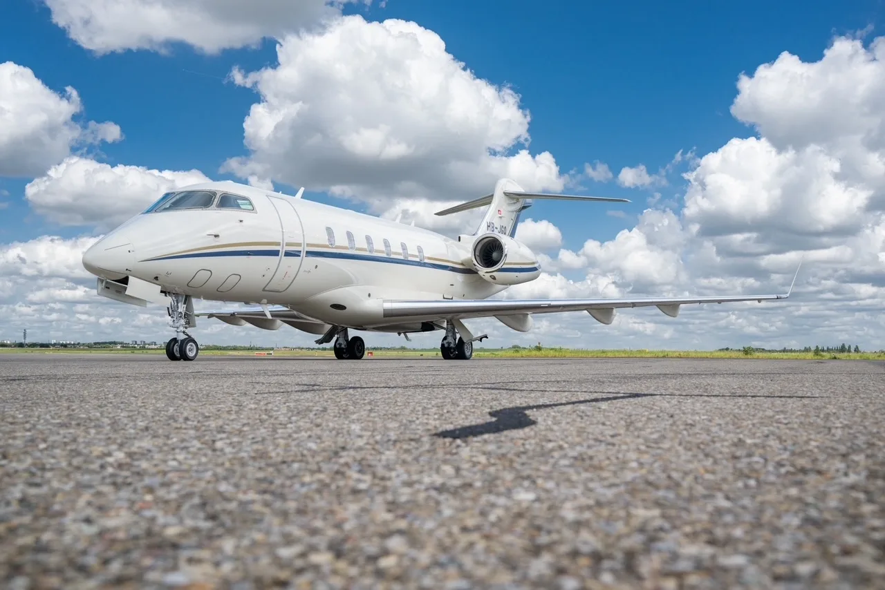 A white Bombardier Challenger 300 business jet with blue and gold stripes parked on the tarmac.