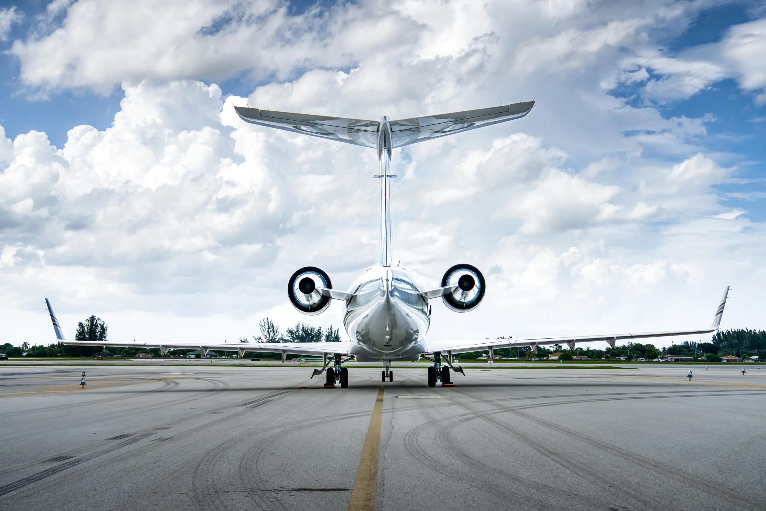 A rear view of a white Bombardier Challenger business jet with gold and black stripes, registration LV-KKF, parked on an airport tarmac.