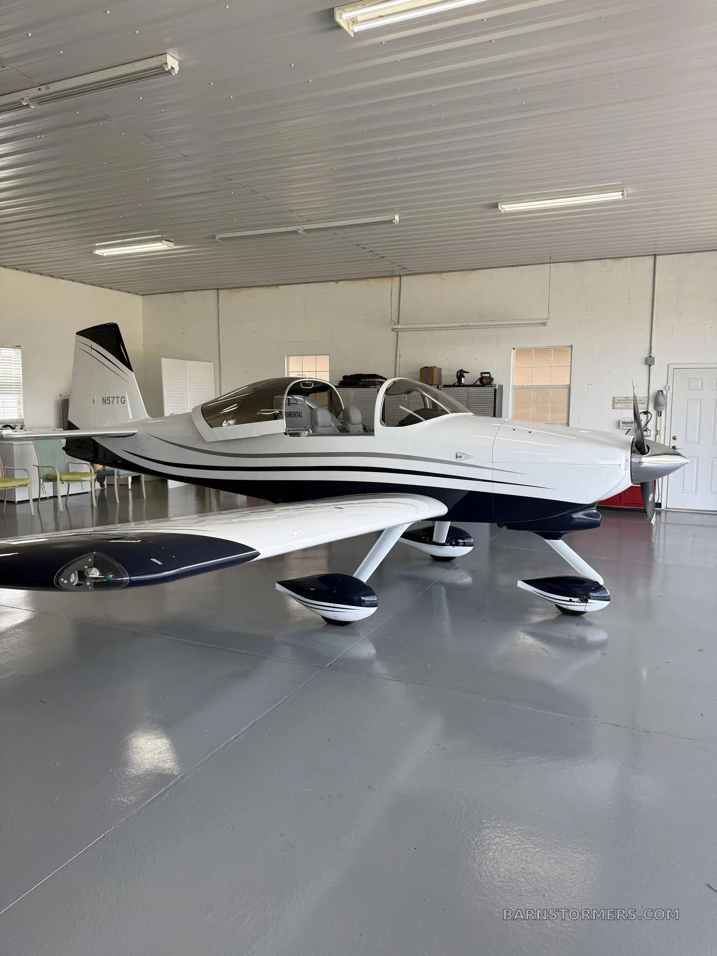 A white and blue Vans RV-7 aircraft with registration N57TG parked inside a hangar.