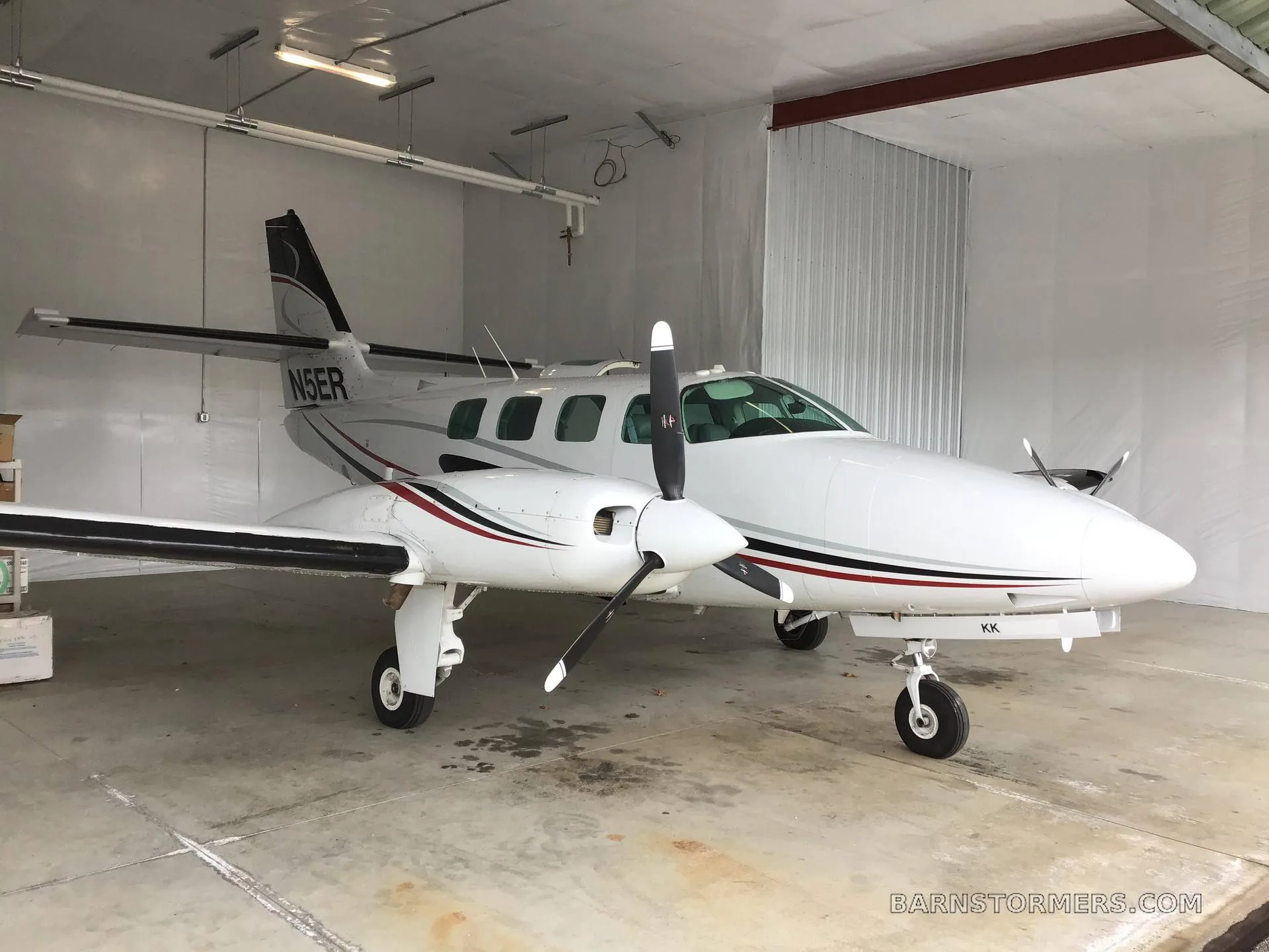 A white twin-engine propeller aircraft with red and black stripes, registration N5ER, parked in a hangar.