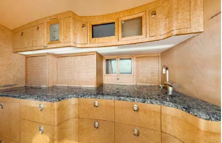A well-appointed aircraft galley with light wood cabinetry, dark granite countertops, and a sink.