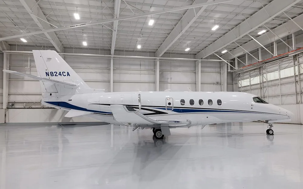 A white business jet with blue and black stripes, registration N824CA, parked in a brightly lit hangar.