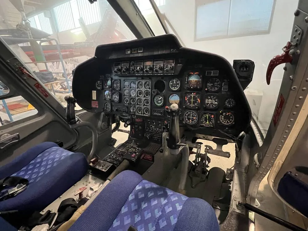 The cockpit of a helicopter, showing the instrument panel and two blue pilot seats.