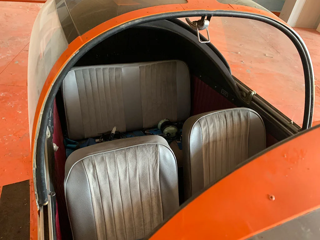 The interior of the aircraft cabin shows two grey front seats and a grey rear bench seat, viewed from above.
