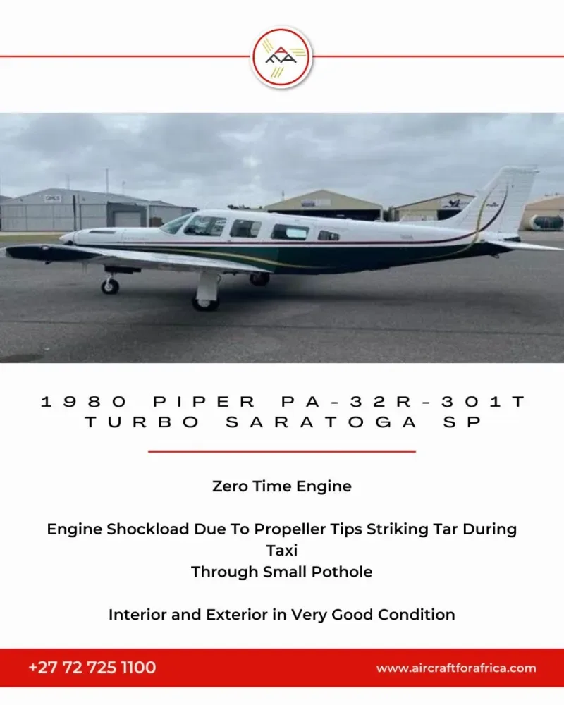 A white Piper PA-32R-301T Turbo Saratoga SP with dark green and gold stripes parked on a tarmac with hangars in the background.