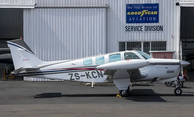 A white twin-engine propeller aircraft with blue and black stripes is parked on an tarmac in front of a hangar.