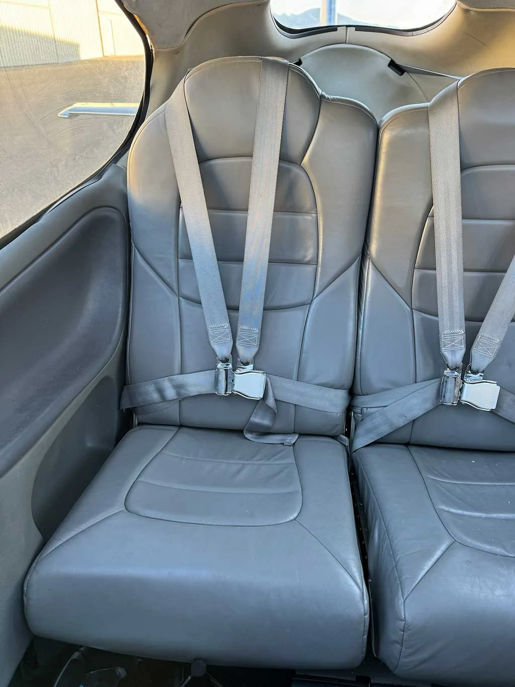 Two gray leather passenger seats with seatbelts in the aircraft cabin.
