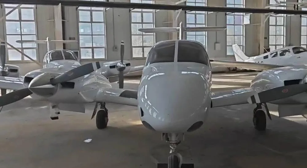 A front view of several white twin-engine propeller aircraft parked closely inside a hangar.