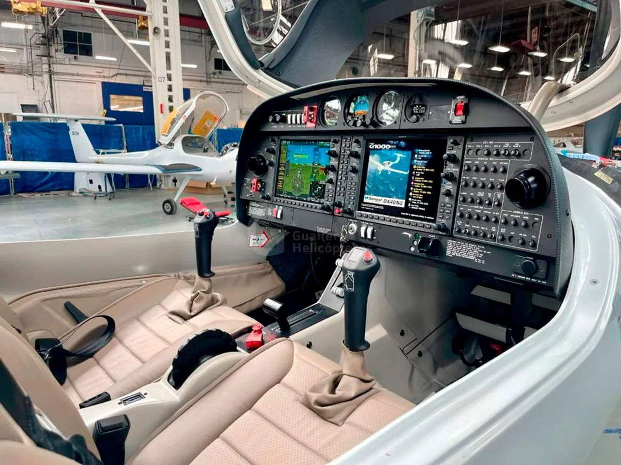 The cockpit of a Diamond DA40 aircraft showing the instrument panel with two large display screens and tan seats.