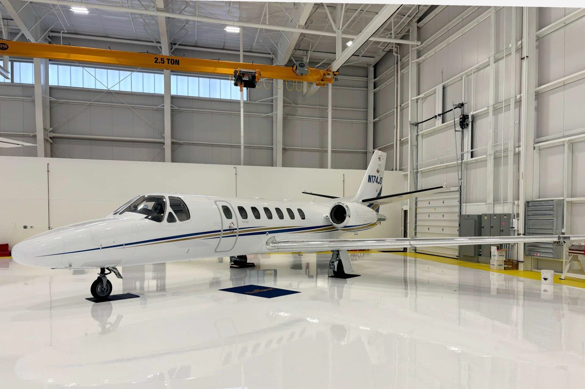 A white business jet with blue and gold stripes, tail number N174JS, parked inside a brightly lit hangar.
