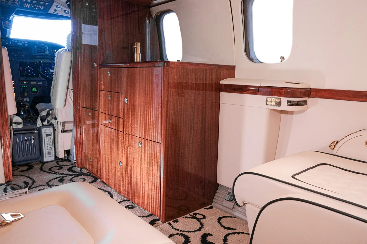 A close-up of the private jet's cabin showing dark wood cabinetry and a cream-colored side panel.