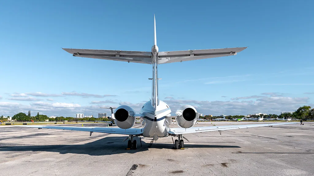 A rear view of the white business jet N9793K parked on an airfield, showing its distinctive T-tail and engines.