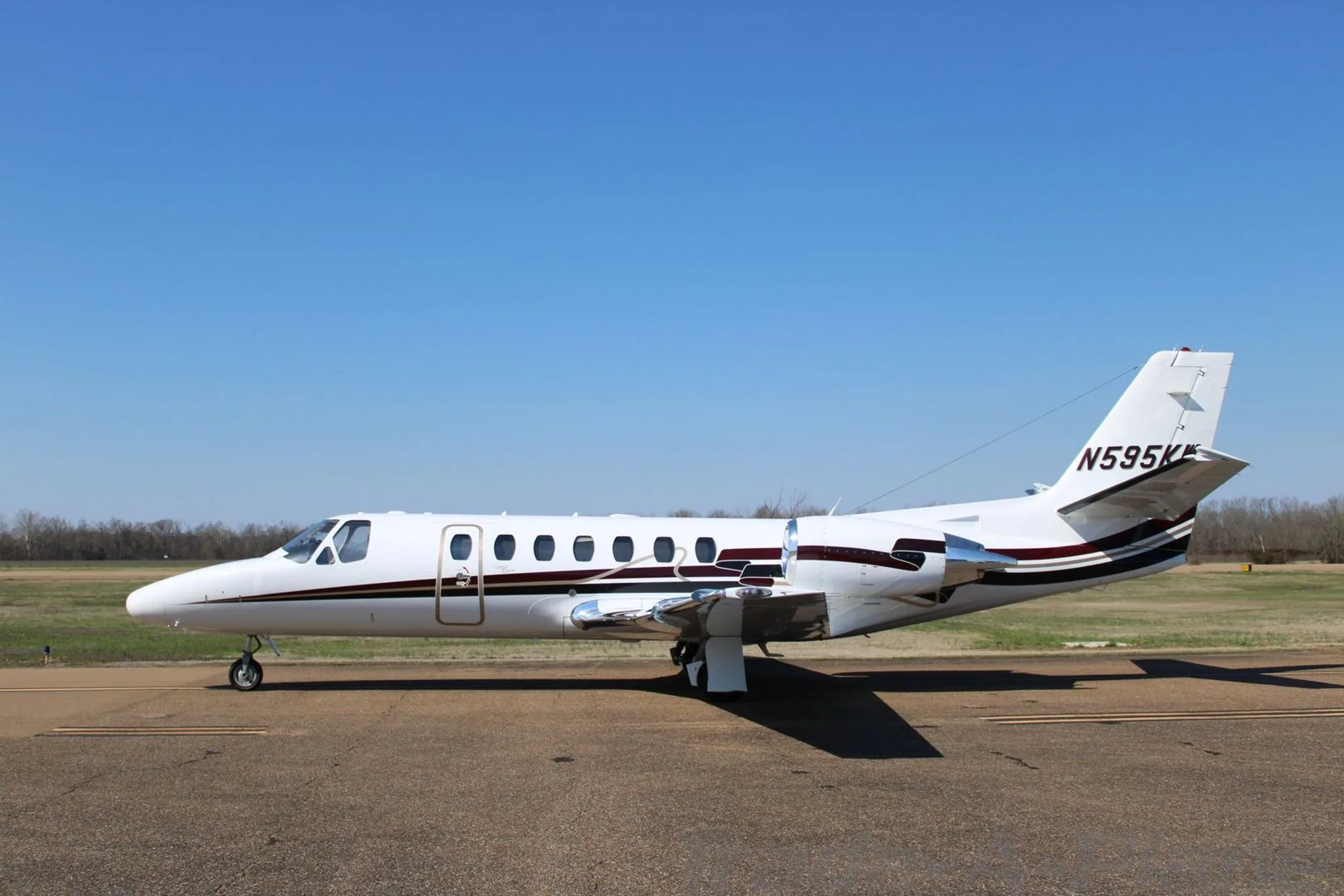 A side profile view of a white Cessna Citation Encore business jet with dark brown and gold stripes on the tarmac.