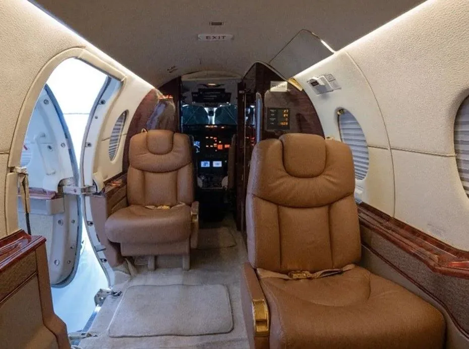 Aircraft interior with two leather seats and an open doorway to the cockpit.