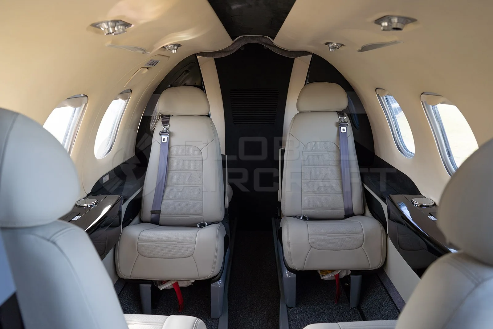 The interior cabin of an Embraer Phenom 100 features two rows of light beige leather seats.